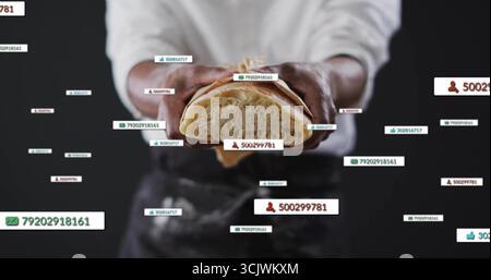 Mid-adult chef wearing apron holding halved loaf in studio, with notifications showing like counts Stock Photo