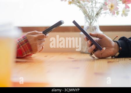Young couple hands using two phones share social media or talking doing shopping online while sit at table. Mobile tech lifestyle concept Stock Photo