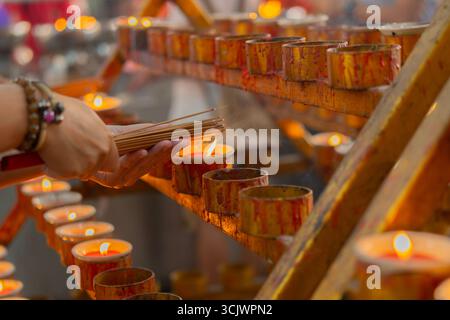 Hand holding incense sticks for worship, Close up shot of people are burning incense from many red candles. Selective focus. Stock Photo