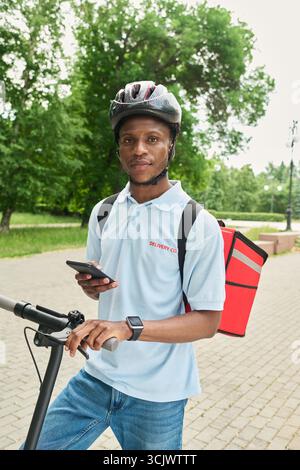Black Man Using Smartphone While Standing with Electric Scooter Stock Photo