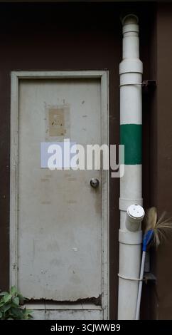 Closed old white wooden door, bottom of the door is broken. There is an empty signboard on the door. Stock Photo