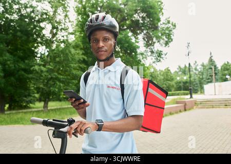 Portrait of Black Man Using Smartphone While Delivering Food Outdoors Stock Photo