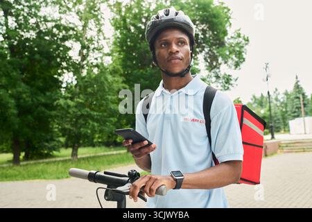 Black Man Using Smartphone While Delivering Food Outdoors Stock Photo