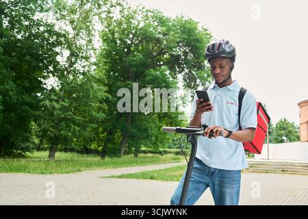 Black Man Using Smartphone While Standing with Electric Scooter Outdoors Stock Photo