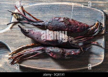 Three baked young beets in skins on a wooden cutting board, close up, top view. Organic vegetables, healthy vegan eating, harvest time Stock Photo