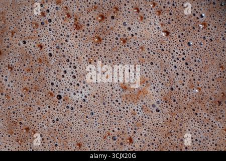 Bubbles on the surface of the cocoa drink with milk on background, close up, top view. Light brown bubbles. Brown cream foam texture Stock Photo