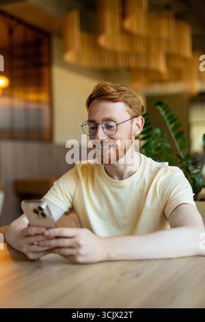 Redhead enjoying free time while using phone in cafe Stock Photo