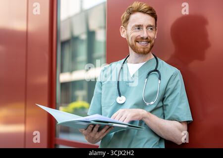 Male healthcare worker in scrubs holding open folder Stock Photo