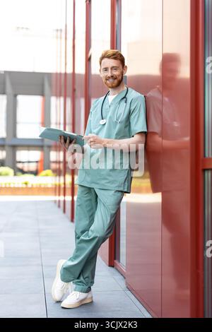 Man physician reading open folder leaning near clinic wall Stock Photo