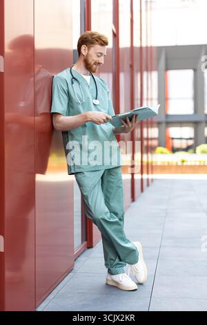 Smiling man doctor studying papers in open medical chart Stock Photo