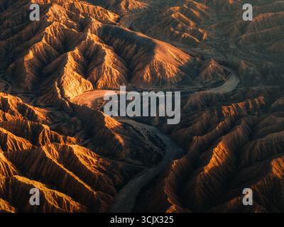 Aerial view of the rugged, sun-kissed canyons carved by a winding river, a landscape painted in hues of gold and shadow, Ak Say, Issyk-Kul Region, Kyrgyzstan. Stock Photo