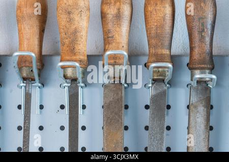 Old vintage rasps with wooden handles hanging on steel wall as background. A set of files and rasps for hand sanding, close up. Hand work tool in work Stock Photo