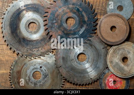 Old circular saw blades and emery wheels on wooden table, close up, top view. Carpentry tools, sawing and grinding equipment Stock Photo