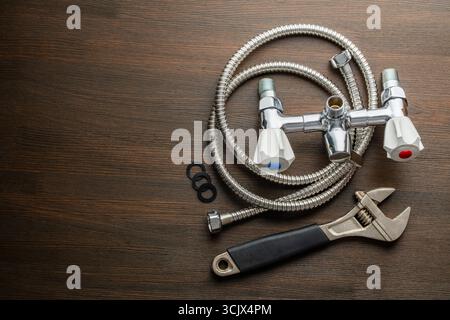 Metal adjustable wrench, faucet with handles, chrome plated shower pipe and rubber gaskets on wooden background, close up, top view, copy space. Plumb Stock Photo