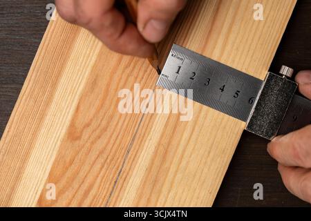 Carpenter steel ruler with limit block for marking or template, close up, top view. The worker hand holds a metal ruler and marks on a wooden board wi Stock Photo