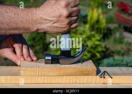 A worker using a hammer nail puller to pull a nail out of a wooden board, close up. Hand tool for working. Multifunction shockproof steel hammer and n Stock Photo