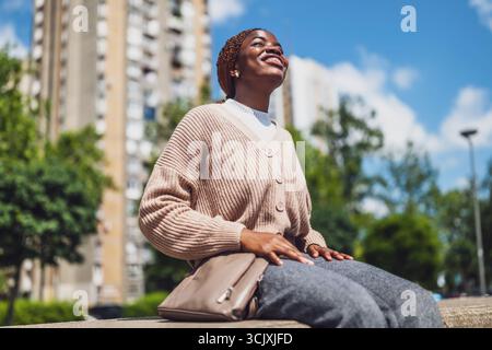Young African American woman sitting in the city park and enjoying sun. Stock Photo