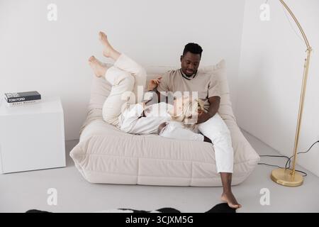 Happy interracial couple relaxes on a comfortable sofa, sharing a tender moment together. Concept of interracial family. Stock Photo