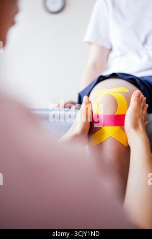 Therapist is applying kinesiology tape on patient's knee, demonstrating rehabilitation techniques in a bright therapy room with a calming atmosphere Stock Photo