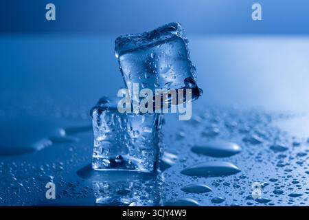 Stacked melting ice cubes surrounded by water puddles, photographed against a blue-toned background. The image symbolizes climate change, global warmi Stock Photo