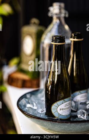 Mini bottles of chilled prosecco on ice in a bowl at an outdoor gathering, ready for a celebration or party, with glassware and décor. Stock Photo
