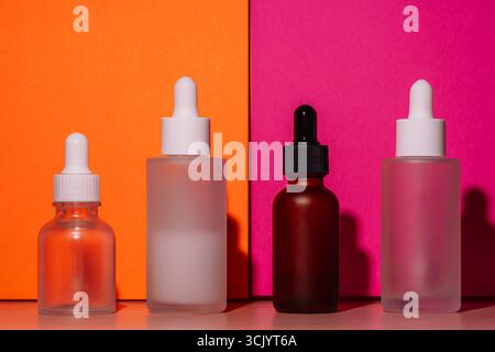 Assorted glass dropper bottles on orange and pink background. Beauty product mockup. Stock Photo