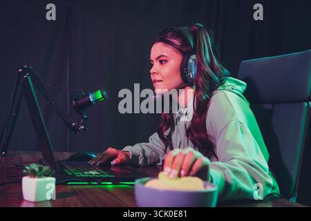Young female gamer streams video games at home with headset and microphone in professional setup during evening Stock Photo