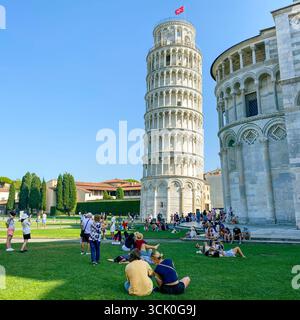 Pisa, Italy - June 26, 2025: Tourists relaxing and taking photos on the green lawn in front of the Leaning Tower of Pisa and the Pisa Cathedral, on a Stock Photo