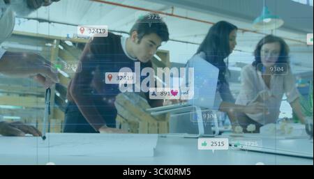 Gesturing professionals examining plans with tablet in open-plan office, with floating icons Stock Photo
