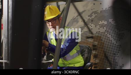 Operating Korean forklift operator steering controls in warehouse, wearing hard hat and safety vest Stock Photo
