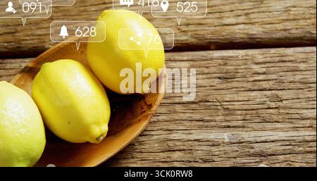 Resting three yellow lemons in bowl on rustic kitchen table overlaid social media icons copy space Stock Photo