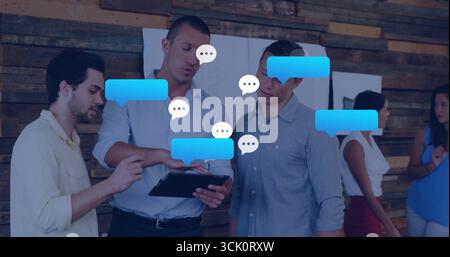 Collaborating colleagues discussing project on tablet in workspace, with digital speech bubbles Stock Photo
