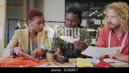 Three designers collaborating in fashion studio, with color palette, swatches and measuring tapes Stock Photo