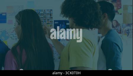 Organizing trio arranging sticky notes and checking charts in planning room, with world map graphic Stock Photo