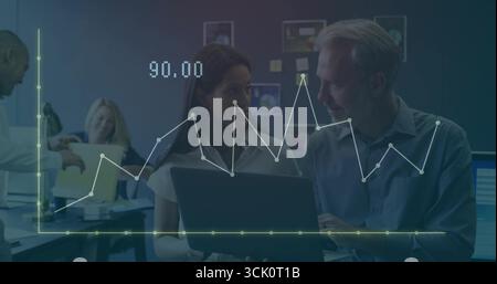 Collaborating colleagues focusing on laptop in open-plan office with charts and data graph overlay Stock Photo