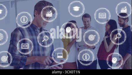 Collaborating office team of five analyzing data on tablet and laptop in office, with digital icons Stock Photo