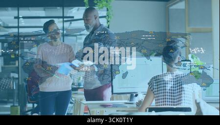 Reviewing two colleagues studying printed documents at office desk, with computer and blue folder Stock Photo