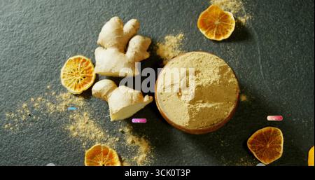 Showing wooden bowl of ginger powder with sliced ginger root, dried citrus slices on stone surface Stock Photo