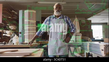 Standing African American carpenter in apron at workshop bench, with lumber, dust extraction hose Stock Photo