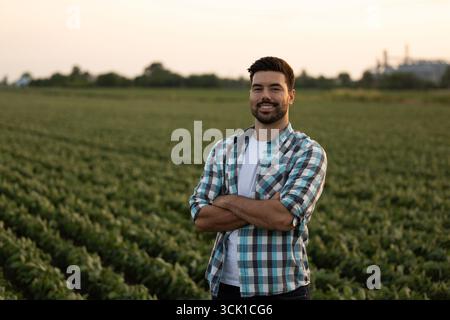 Handsome farmer in plaid shirt standing in a field with his arms crossed confidently Stock Photo