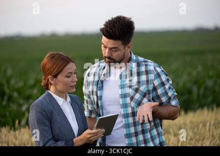 Farmer and businesswoman standing in a field using digital tablet while having serious discussion Stock Photo