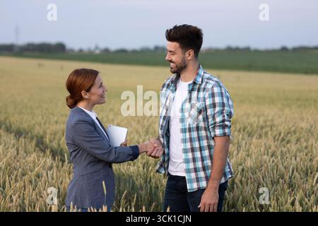 Handshake between a male farmer and woman in formal attire while standing in a wheat field. Agricultural business concept Stock Photo