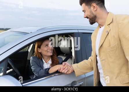 Handshake between businesswoman sitting in driver's seat and male salesman standing next to car he sold. Succesfull automobile purchase was made Stock Photo