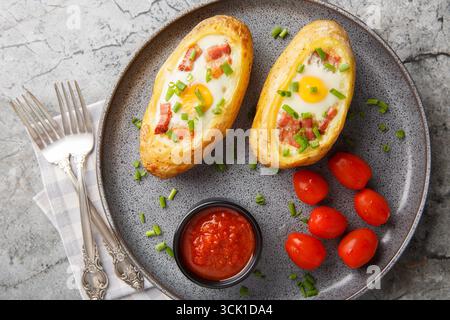 Potatoes stuffed with bacon, greens and eggs closeup on the plate on the table. Horizontal top view from above Stock Photo