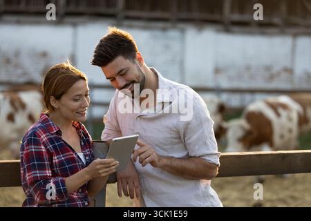 Young man and woman on a farm, relaxed as they look at records on cows on digital tablet Stock Photo