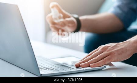 Device disinfection. Male hand using disinfectant spray and cloth for cleaning laptop keyboard Stock Photo