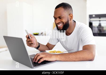 Black man using pc and smartphone having breakfast at home Stock Photo