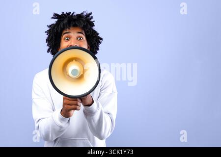 Emotional black teenager making announcement with megaphone on blue studio background Stock Photo