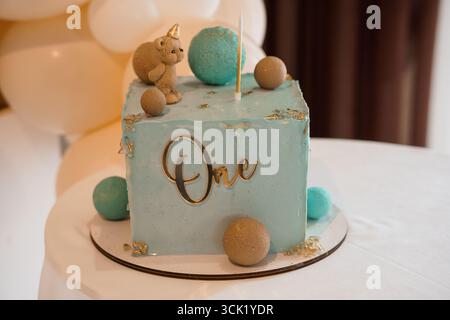 Adorable first birthday cake decorated with a unicorn theme features a blue square frosting, a One topper, a cute teddy bear figurine, and colorful ma Stock Photo
