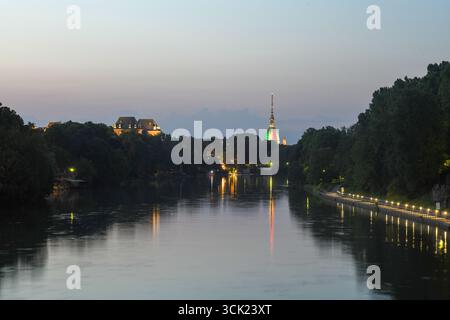 A stunning long exposure shot of the Po River in Turin at dusk. The image features the river's peaceful surface mirroring the lights along the tree-li Stock Photo